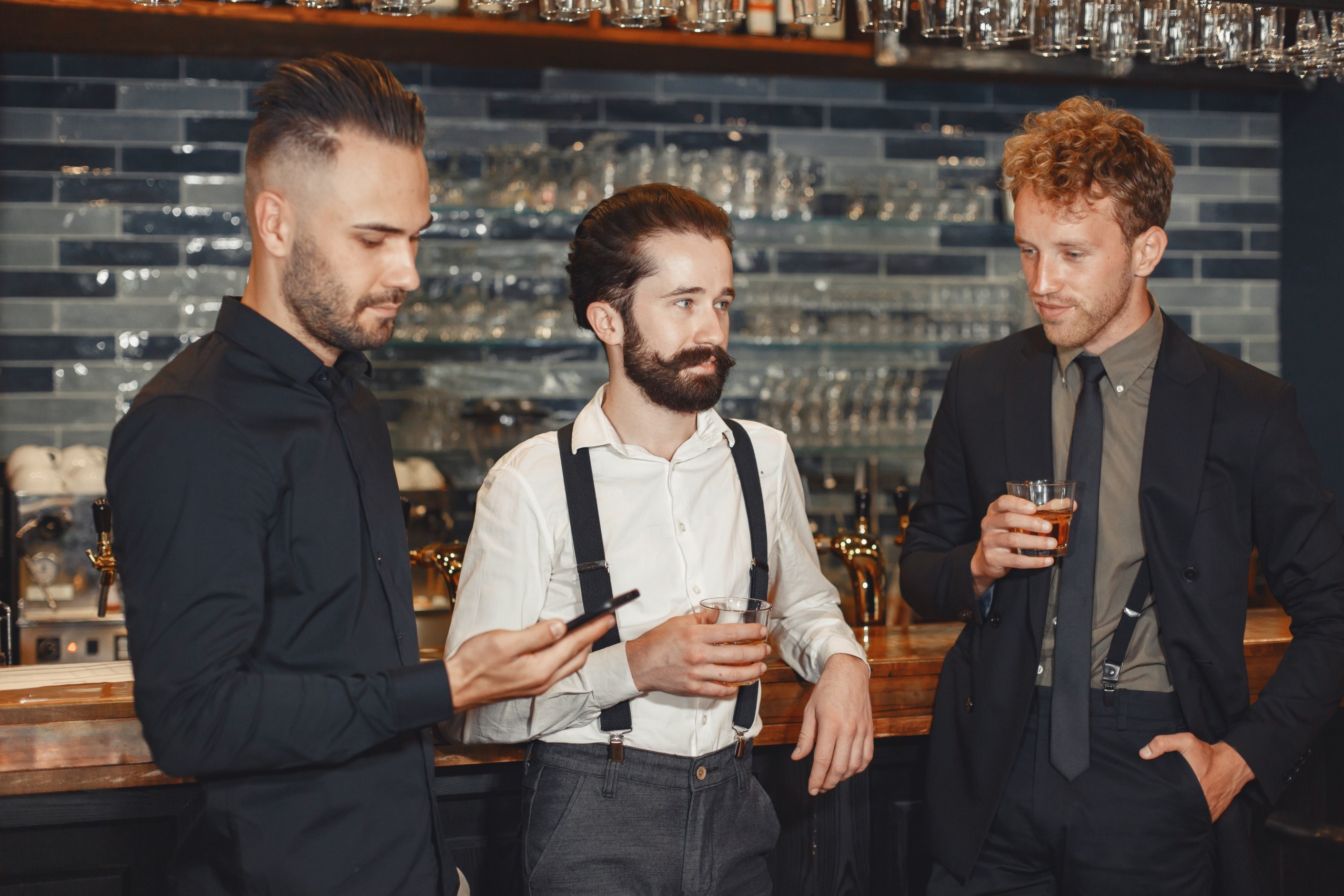 meeting-with-best-friends-three-happy-young-men-casual-wear-talking-drinking-beer-while-sitting-bar-together-man-holding-phone-his-hands